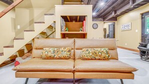 Un salon moderne avec un canapé, une bibliothèque, un escalier et un jeu de fléchettes.