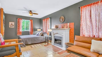 A room with a bed, a sofa, a fireplace, and a ceiling fan.