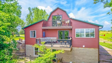 A two-story house with a balcony, a staircase leading to the entrance, and a view of the surrounding greenery.