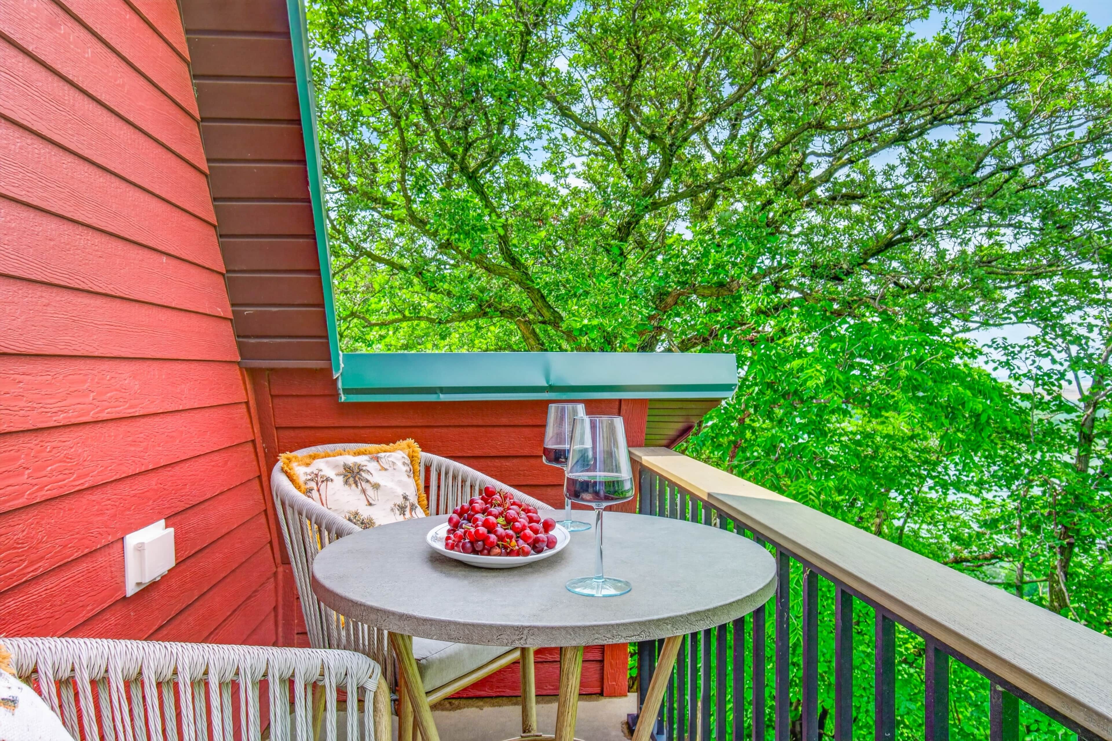 Een balkon met een tafel, een stoel, een schaal fruit en een wijnglas.