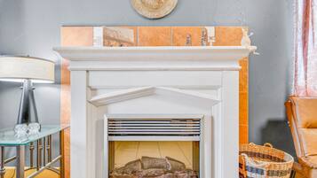 A fireplace with a tiled mantle, a glass table with crystal, and a wicker basket.