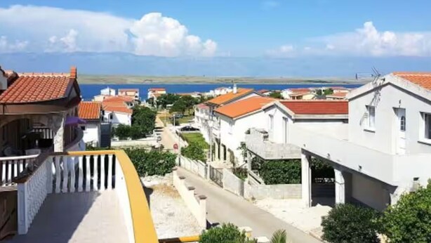 A coastal residential area with houses featuring red-tiled roofs, a clear sky, and a view of the sea. - Two Bedroom Apartment with Terrace and Sea View (Vir)