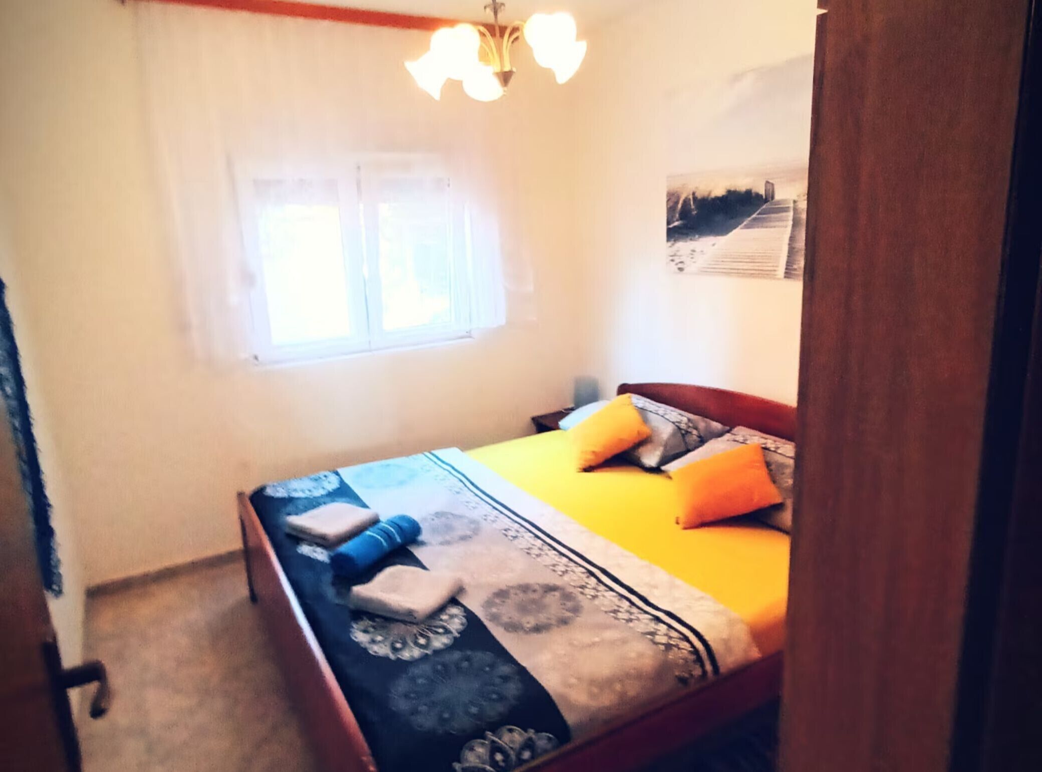 A bedroom with a bed, a window, and a wall-mounted light fixture.