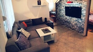 Un salon comprenant un canapé, une table basse, un mur en pierre, un téléviseur et un luminaire suspendu.