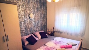 Une chambre à coucher comprenant un lit, une armoire, une lampe fixée au mur et une fenêtre avec des rideaux.