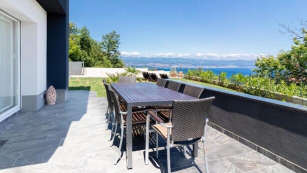 Un patio con mesa y sillas, vista al mar y un edificio moderno.