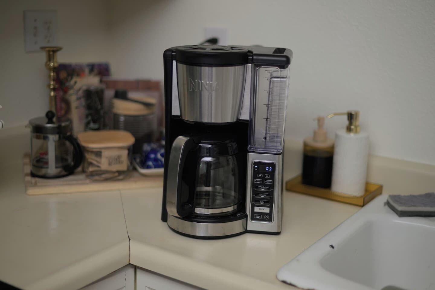 Una cafetera con pantalla digital, un lavamanos pequeño y una tabla de madera con un molinillo de café.