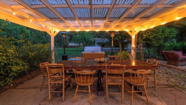 Una terrazza esterna con un tavolo e sedie di legno, un barbecue e luci a stringa.