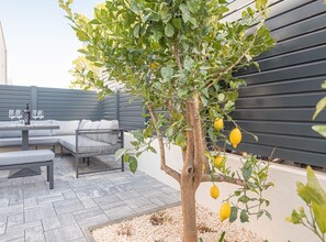 A modern outdoor seating area with a table and chairs, a cushioned bench, and a small tree with lemons. - Three Bedroom Villa with Outdoor Swimming Pool (Vodice)