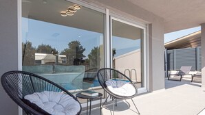 Un balcón con dos sillas de mimbre, una mesita y una puerta de cristal que da a una zona de piscina.