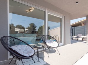 A balcony with two wicker chairs, a small table, and a glass door leading to a pool area. - Three Bedroom Villa with Outdoor Swimming Pool (Vodice)