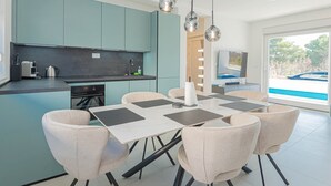 Una cocina moderna con armarios verde azulado, un comedor con mesa y sillas, y un ventanal con vistas a un barco.