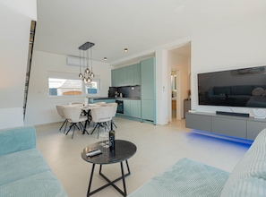 A modern living room with a TV, a dining area with chairs, and a kitchen with teal cabinets. - Three Bedroom Villa with Outdoor Swimming Pool (Vodice)
