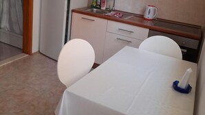 Ein Essbereich mit Tisch, Stühlen, einer Küche im Hintergrund und einem Fliesenboden.