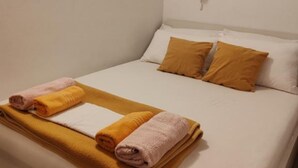 Ein Einzelbett mit zwei Kissen, einer Decke und zwei gerollten Handtüchern.