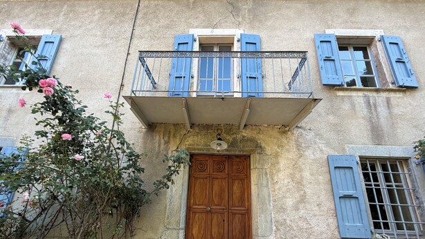 A building with a wooden door, blue shutters, and a balcony with a metal railing.