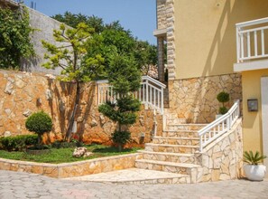 A stone staircase leading to a building with a yellow facade, surrounded by greenery and a stone wall. - Two Bedroom Apartment with Terrace and Pool (Trogir)