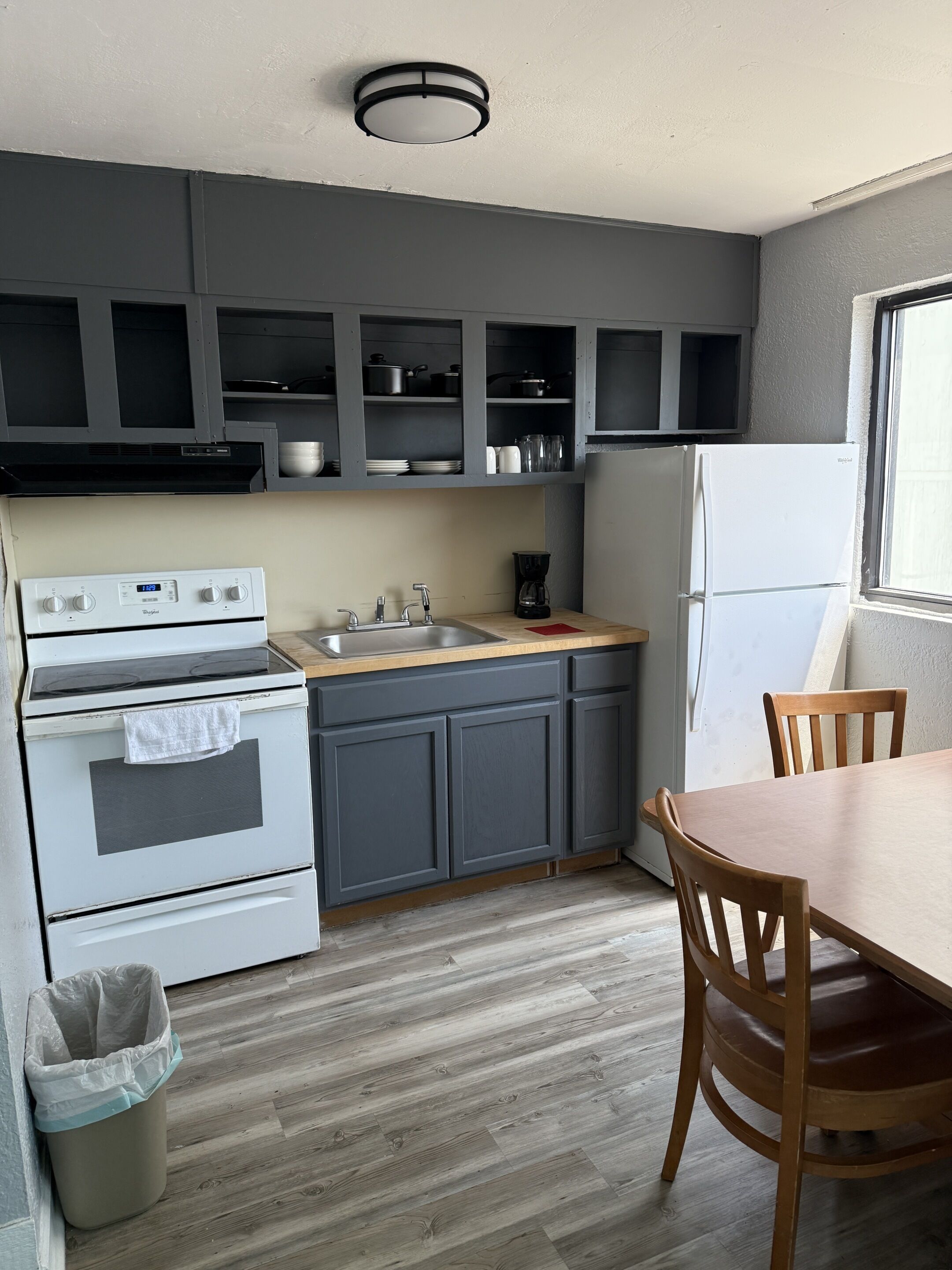 Une cuisine équipée d’une cuisinière, d’un évier et de placards, une table à manger avec des chaises et une fenêtre.