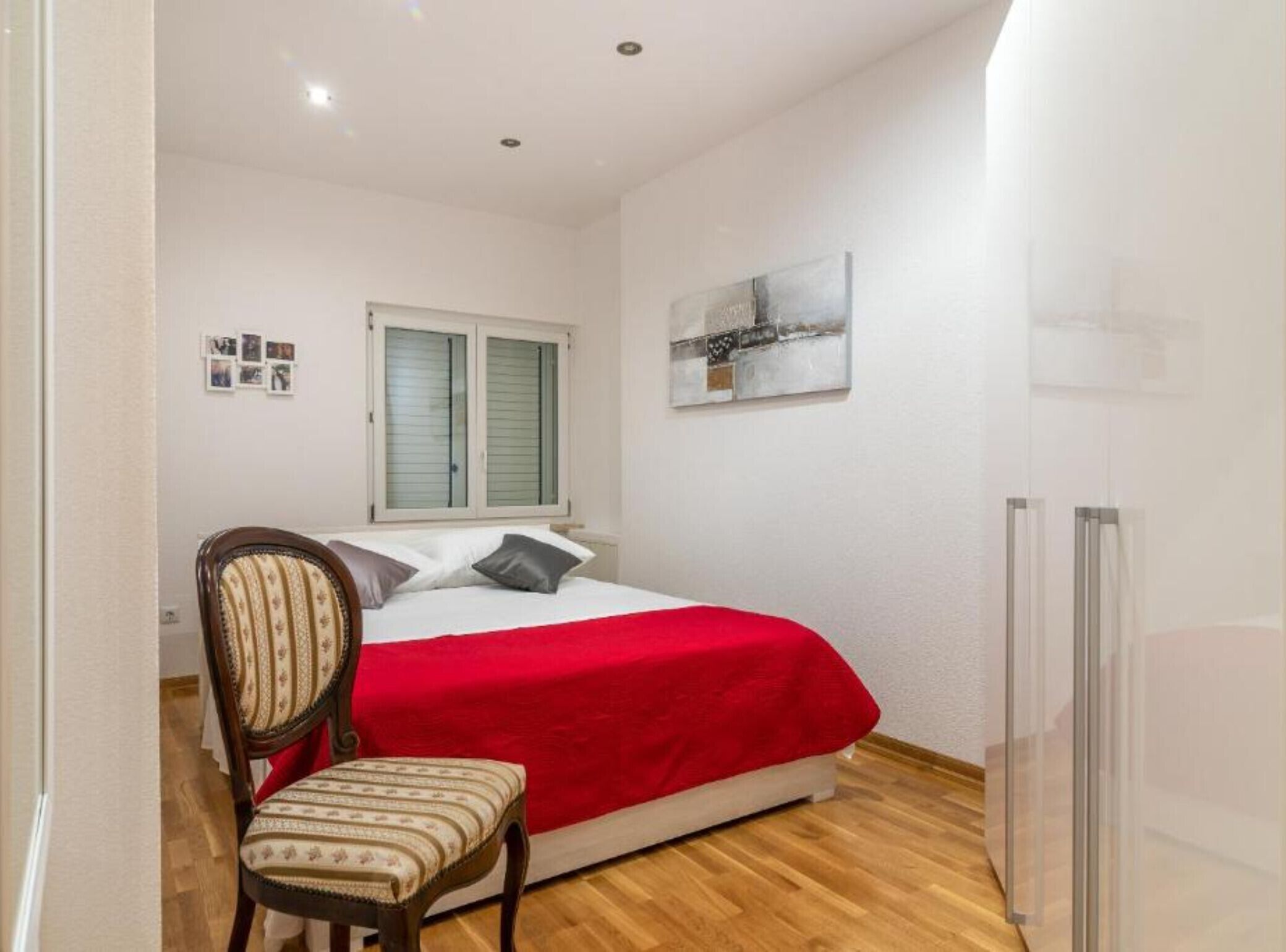 Una camera da letto con un letto, una sedia, una finestra con persiane, un termosifone e un quadro appeso al muro.