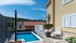 A swimming pool with a stone deck, a potted plant, and a white chair. - Deluxe Three Bedroom Apartment with Balcony and Pool (Trogir)