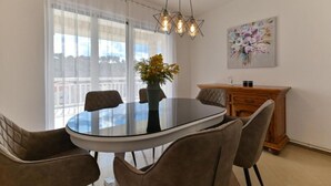 A dining area with a glass table, four chairs, a vase with flowers, a wooden cabinet, and a painting on the wall. - Deluxe Three Bedroom Apartment with Balcony and Pool (Trogir)