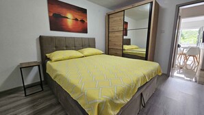 Quarto com cama, mesa de cabeceira, espelho e uma pintura de pôr do sol.
