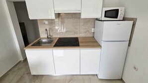 Uma cozinha compacta com armários brancos, micro-ondas embutido e geladeira.