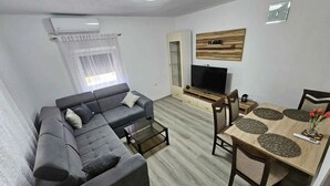 Ein Wohnzimmer mit Ecksofa, Fernseher, Esstisch mit Stühlen und einem kleinen Couchtisch.