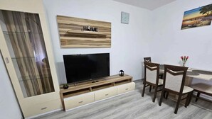 Ein Wohnzimmer mit Fernseher, einer Holz-Unterhaltungsecke und einem Essbereich mit Stühlen und Tisch.