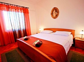 A hotel room with a bed, two bedside tables, a nightstand, a window with curtains, and a framed picture on the wall. - Superior Two Bedroom Apartment with Terrace (Supetar)
