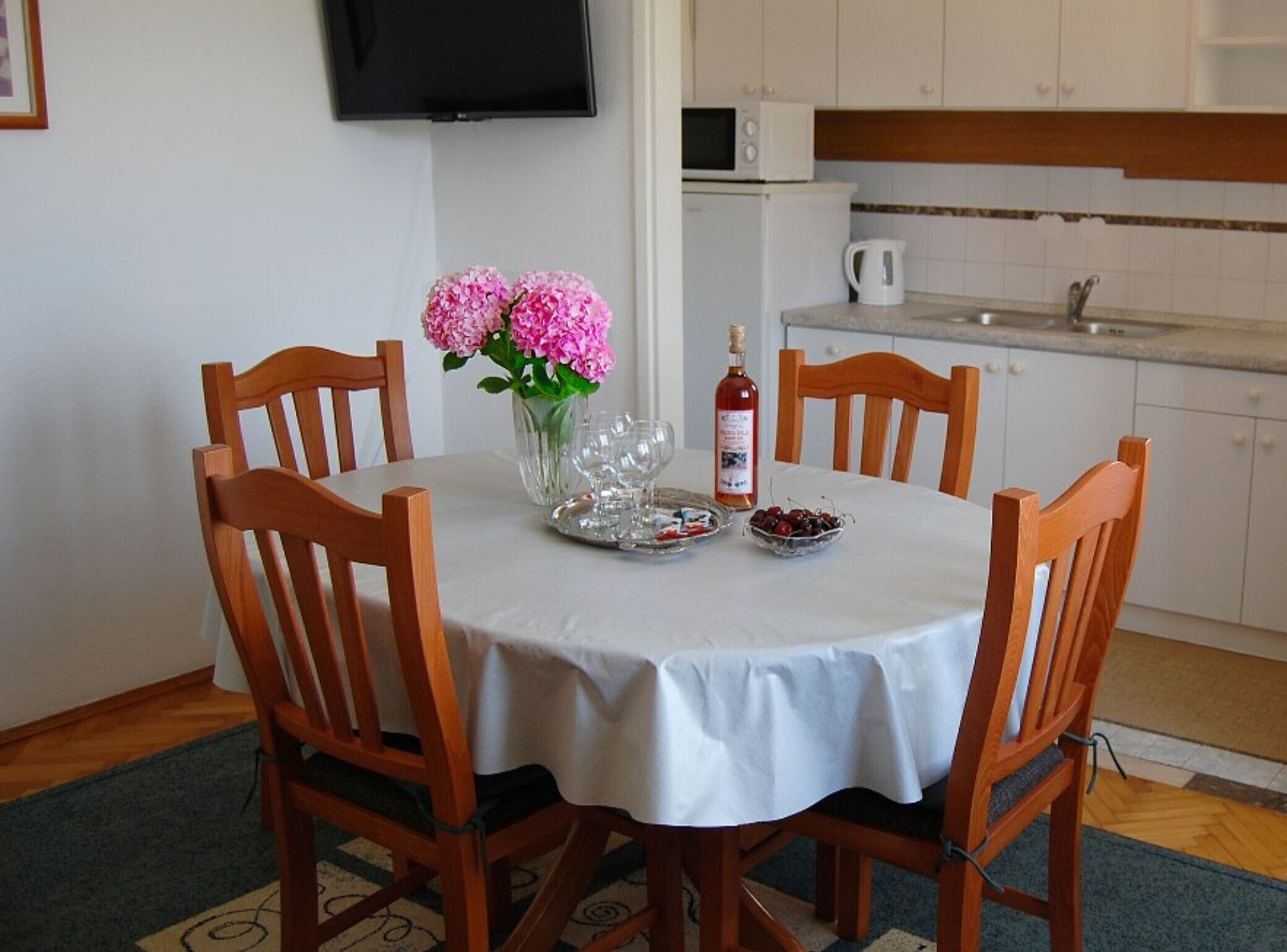 A dining table with chairs, a vase with flowers, a bottle, and a bowl of fruit.