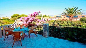 Eine Terrasse mit Korbmöbeln und einem Tisch, umgeben von Steinplatten und einem Metallgeländer.