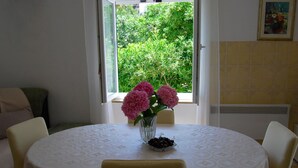 Et rundt bord med et mønstret borddække, omgivet af fire stole, en vase med pink blomster og en skål med kirsebær.