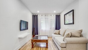Ein Wohnzimmer mit einer Couch, einem Couchtisch, einem Fernseher und einem Fenster mit Vorhängen.
