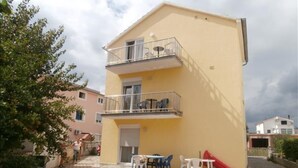 Ein zweistöckiges Gebäude mit einem Balkon, einer Terrasse mit Gartenmöbeln und einem gepflasterten Innenhof.