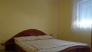 Ein Einzelbett mit Holz-Kopfteil in einem Zimmer mit gelben Wänden und einem Fenster mit Rollo.