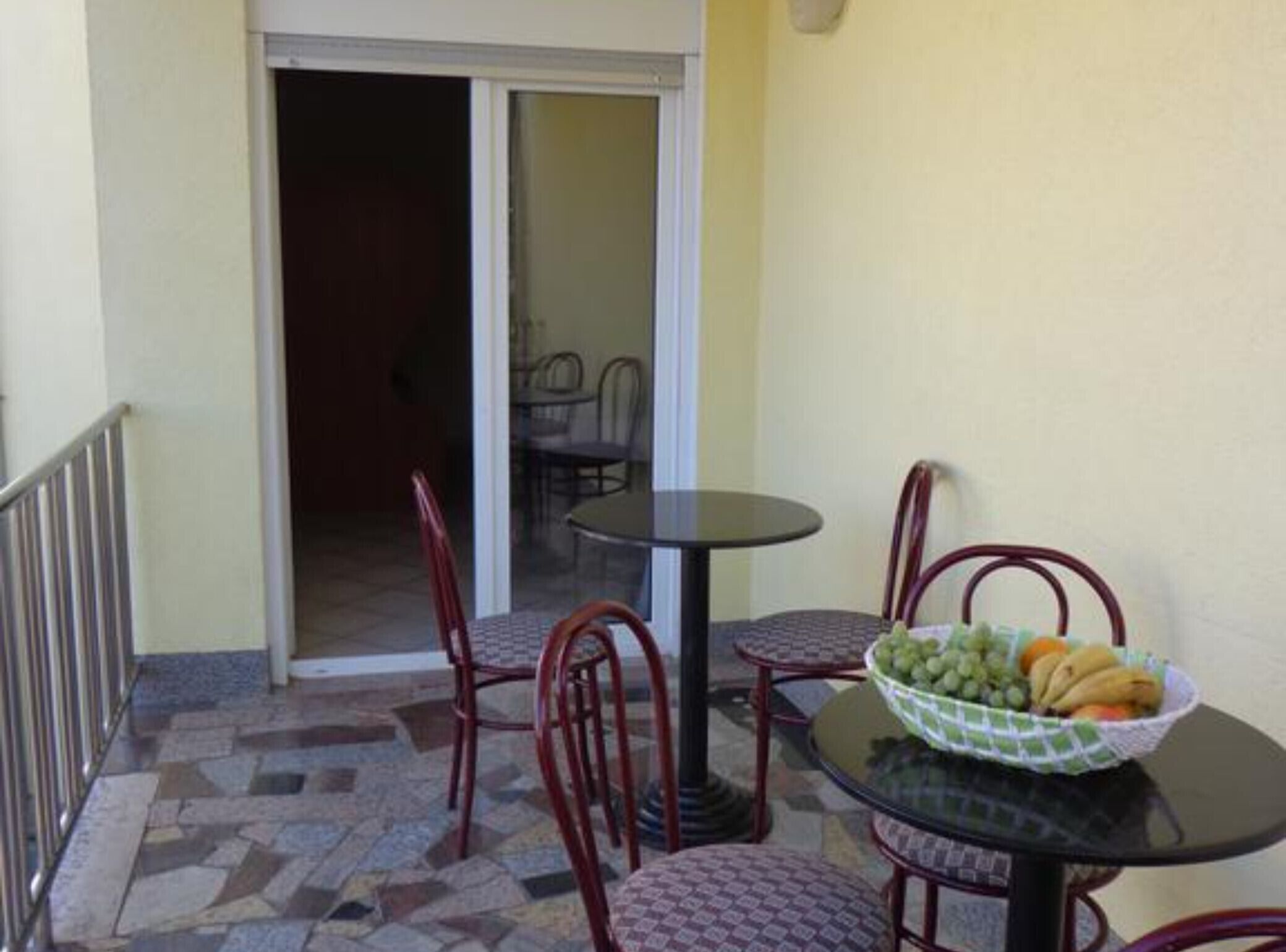 A patio area with a table and chairs, a bowl of fruit, and a sliding glass door leading to an indoor space with additional seating.