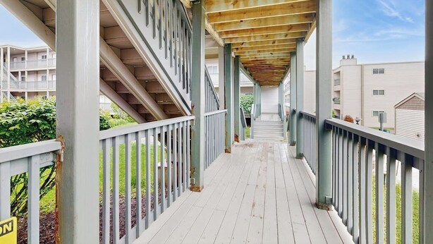 Un espace extérieur abrité, doté d’un plancher en bois et de rampes en métal, qui mène à un escalier.