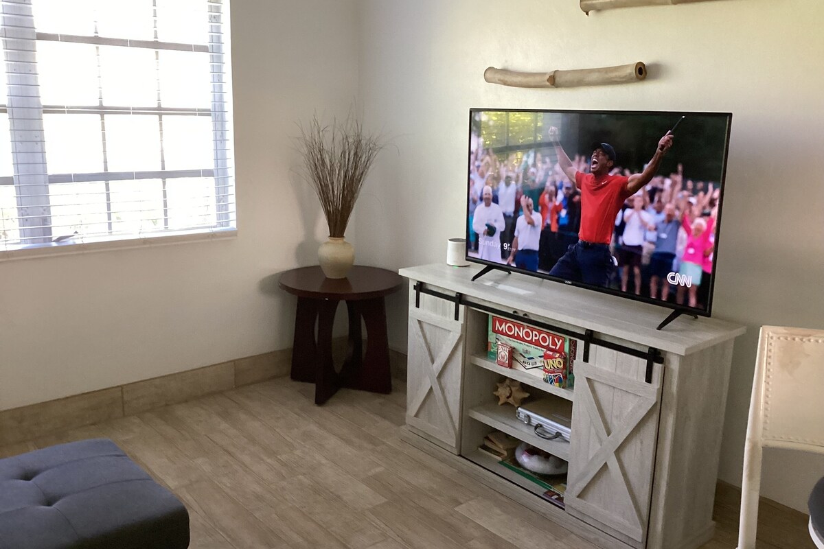 Un soggiorno con televisione su un mobile, un tavolino rotondo con un vaso e un armadio pieno di giochi da tavolo.