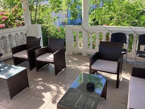 An outdoor patio with wicker furniture and a glass table, surrounded by a white fence and lush greenery. - Colwin's Place  (Cockburn Town)