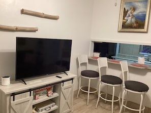 Un comedor con televisión, sillas, una mesa y un cuadro en la pared.
