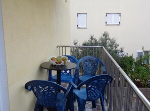 Un balcon avec des chaises bleues et une table, un bol de nourriture, et un bâtiment avec deux fenêtres en arrière-plan.