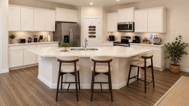 A kitchen with white cabinets, a stainless steel refrigerator, a microwave, and a large island with stools.