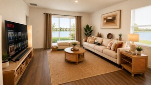 A living room with a TV, a sofa, a coffee table, and a view of a body of water.