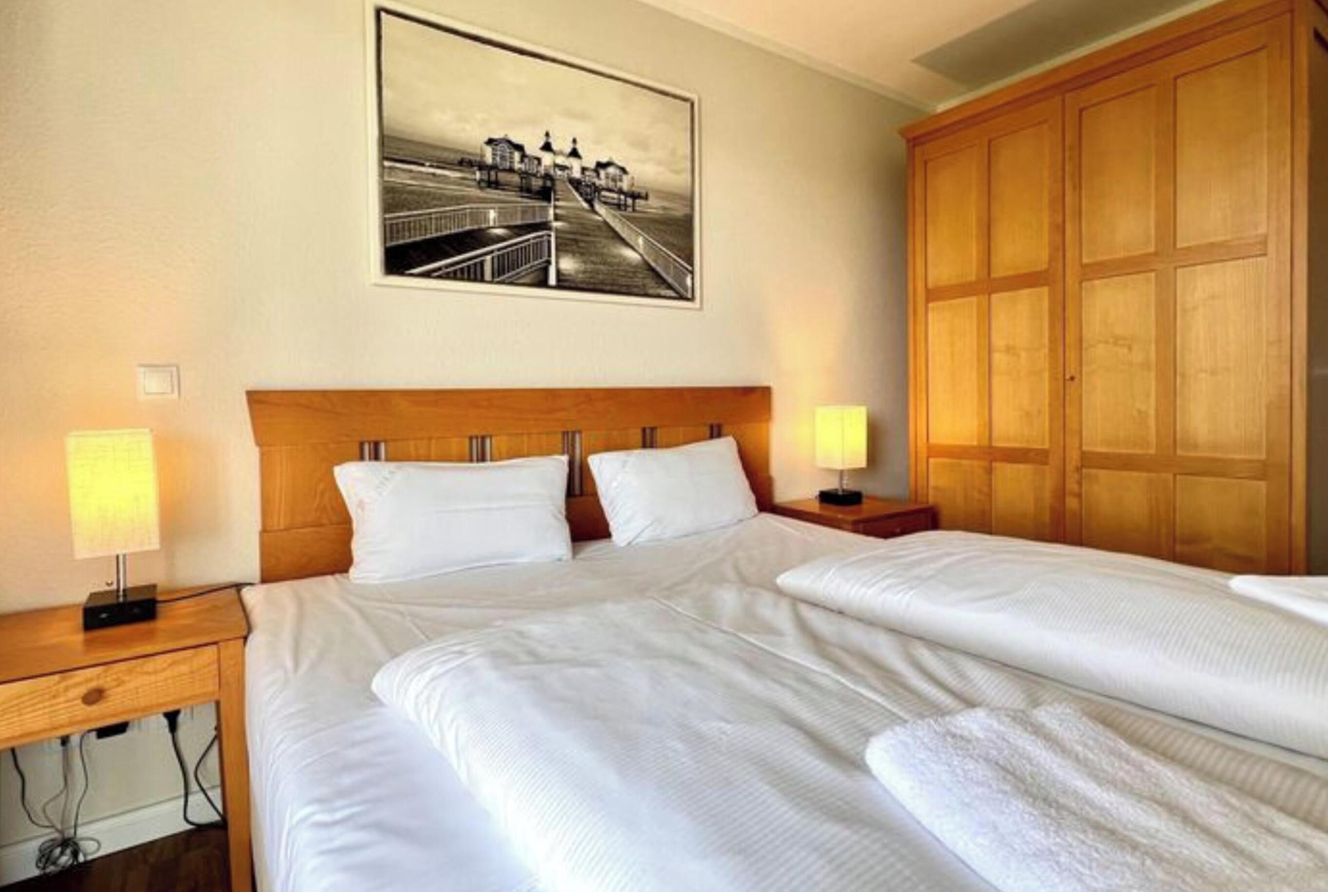 Ein Hotelzimmer mit einem großen Bett, zwei Nachttischen, einem Holzschrank und einem gerahmten Bild an der Wand.