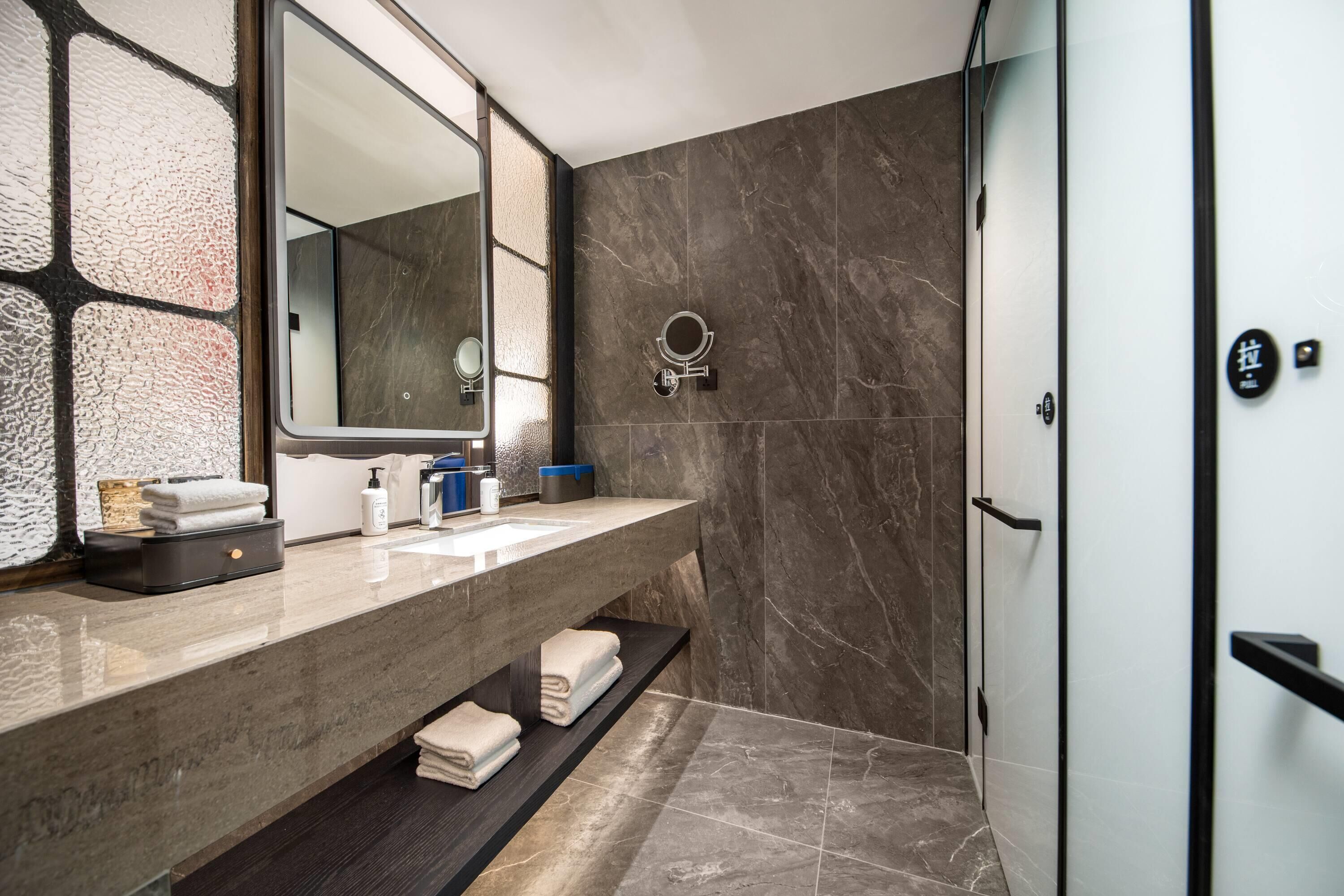 A modern bathroom with a marble vanity, a large mirror, and a shower area.