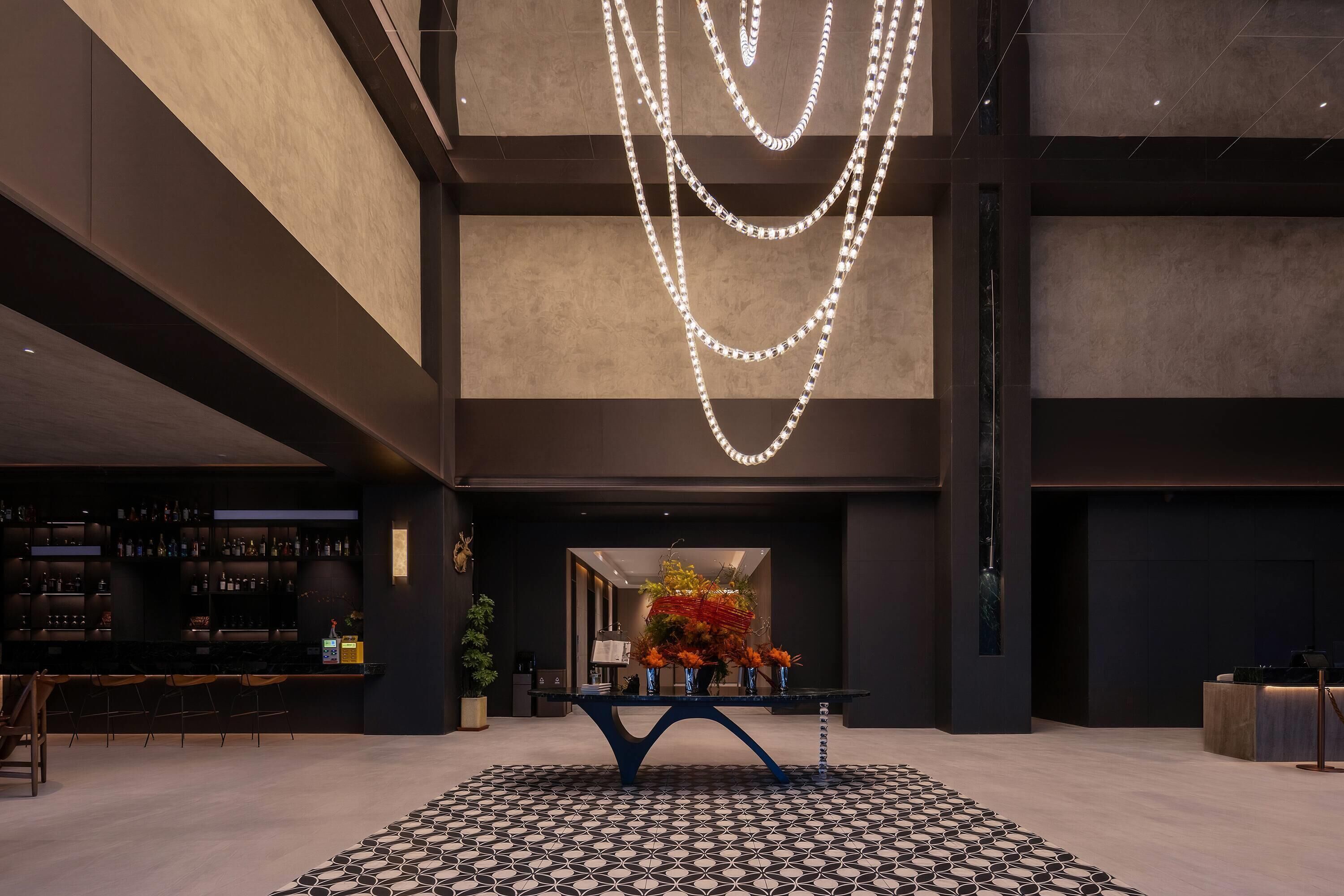 A modern lobby with a bar area, a patterned floor, and a decorative light installation.