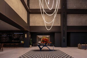 Um lobby moderno com área de bar, piso estampado e uma instalação de luz decorativa.