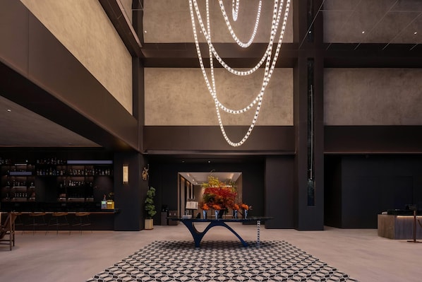 Un vestíbulo moderno con una zona de bar, suelo estampado e instalación de luces decorativas.