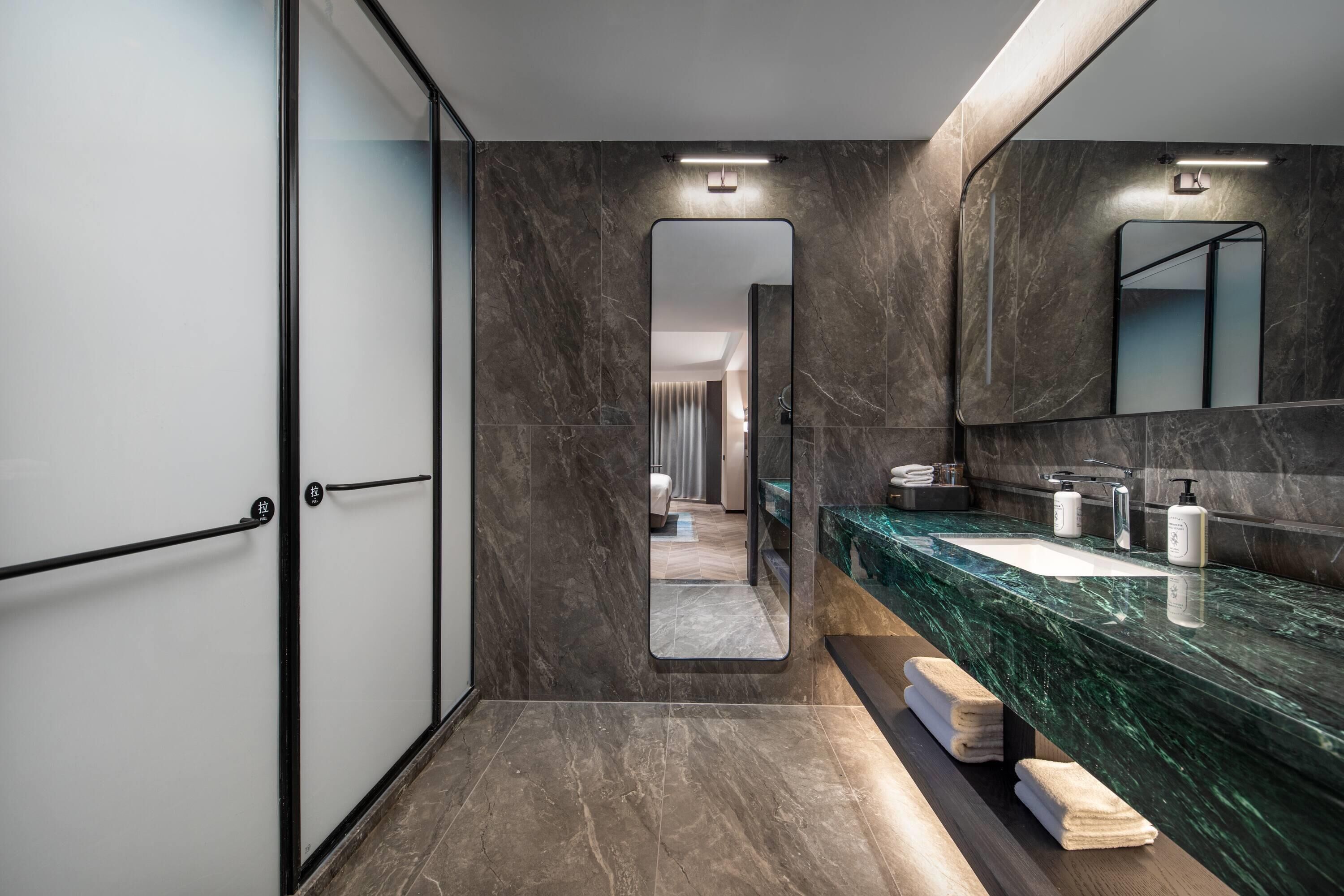 Un baño moderno con un espejo grande, baldosas de mármol oscuro y un tocador elegante.